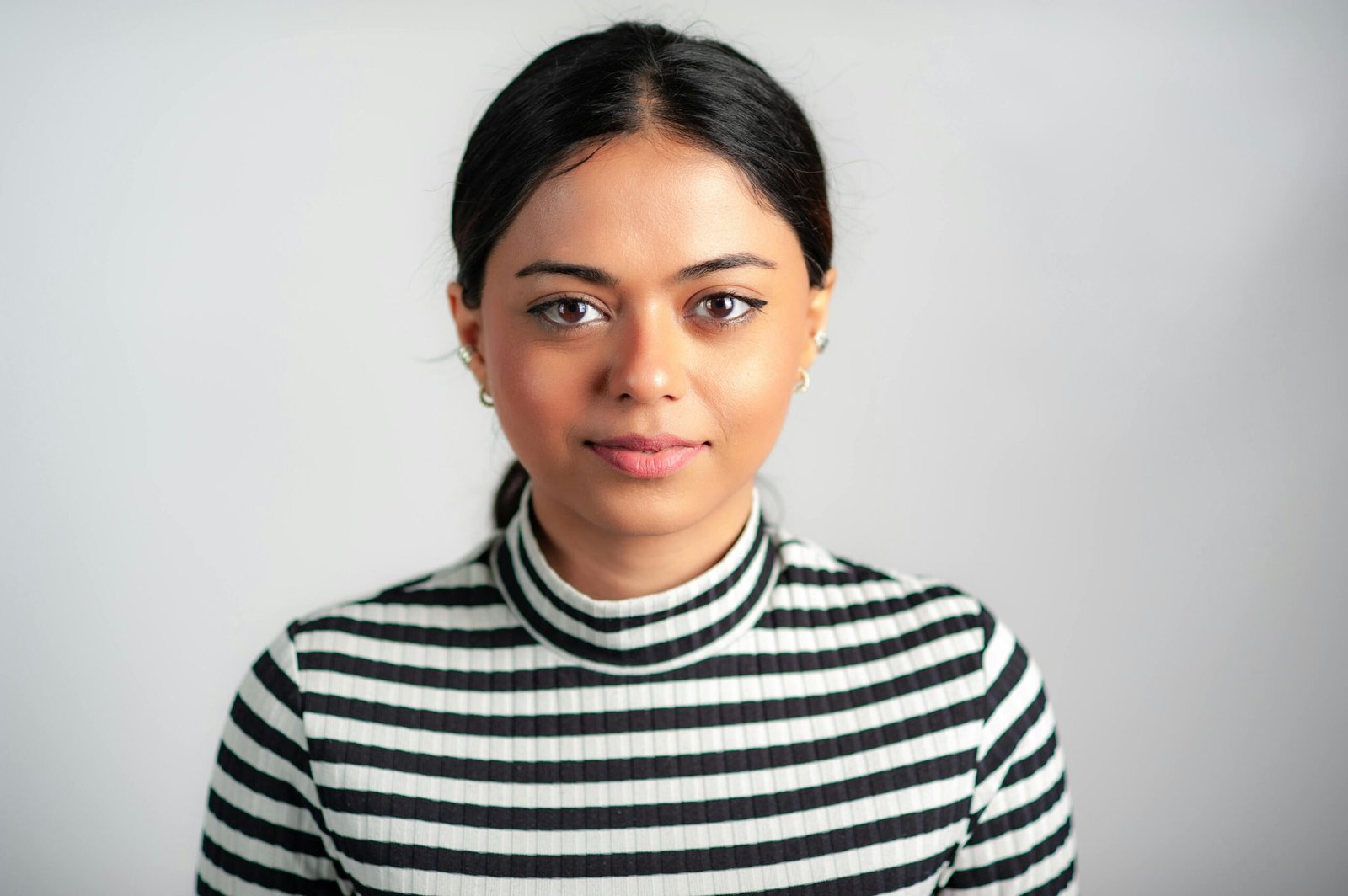 Elegant portrait of an adult woman in a striped turtleneck against a white background.